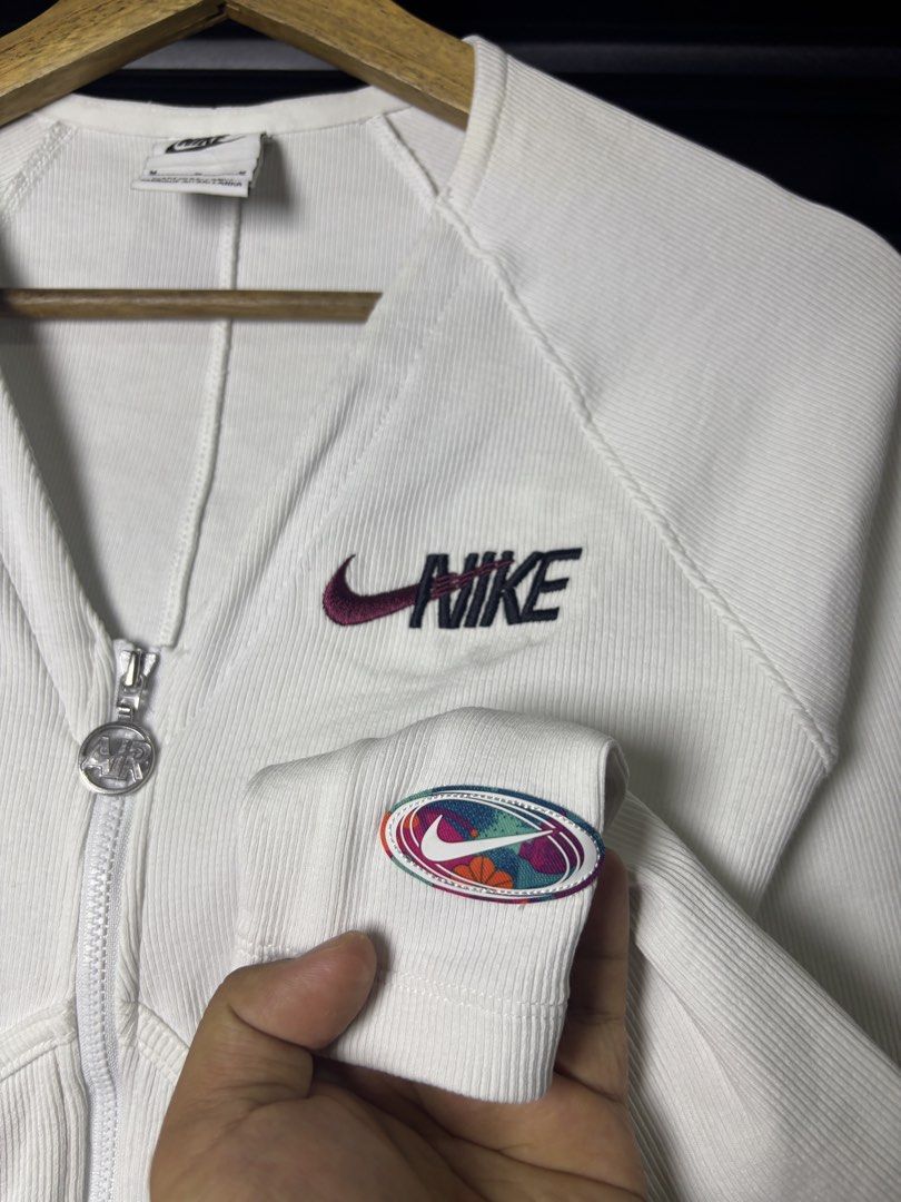 Nike White Zip-Up Jacket "Leap High" (Category: Coats, Jackets and Outerwear) located in San Jose. Submitted by galitsabarat (Listing ID 1458887920, Image 3). Description: - White Nike zip-up jacket - Size: Medium (M) - Features a 'Leap High' graphic on the front - Ribbed texture throughout the jacket - Colorful Nike logo detail on the sleeve - Zipper pull includes 'Air' detail.
