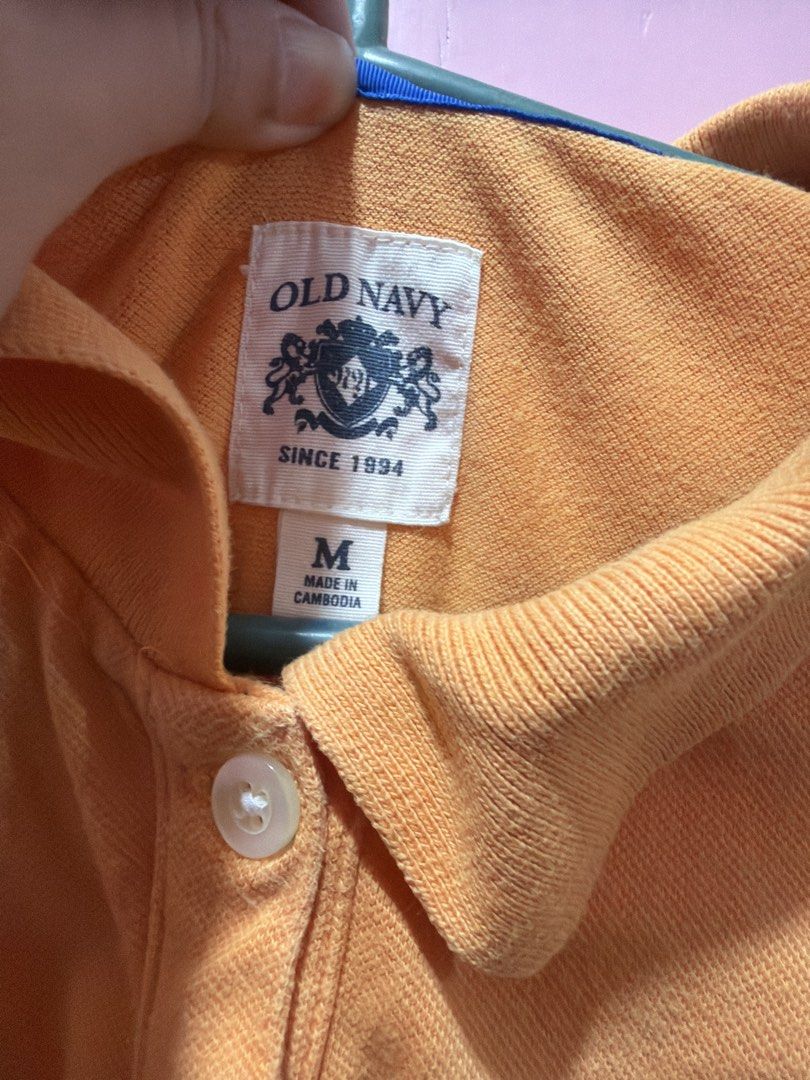Old Navy Orange Polo Shirt Size M (Category: Shirts) located in Muntinlupa City. Submitted by lybns (Listing ID 1458810552, Image 3). Description: - Orange polo shirt from Old Navy - Size: Medium (M) - Features a small blue embroidered deer logo on the chest - Classic two-button placket - Made in Cambodia - Ideal for casual wear.