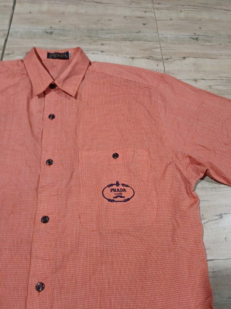 Prada Orange Gingham Short Sleeve Button Up Shirt (Category: Tshirts & Polo Shirts ) located in Bansalan. Submitted by tripandthrift (Listing ID 1458813002, Image 2). Description: - Authentic Prada orange and white gingham shirt - Short sleeves with a classic button-up front - Features a chest pocket with embroidered Prada logo - Made from 100% premium cotton - Tag size: 39/15.5 +XL 23/30 Dimes - Ideal for a stylish and casual look.