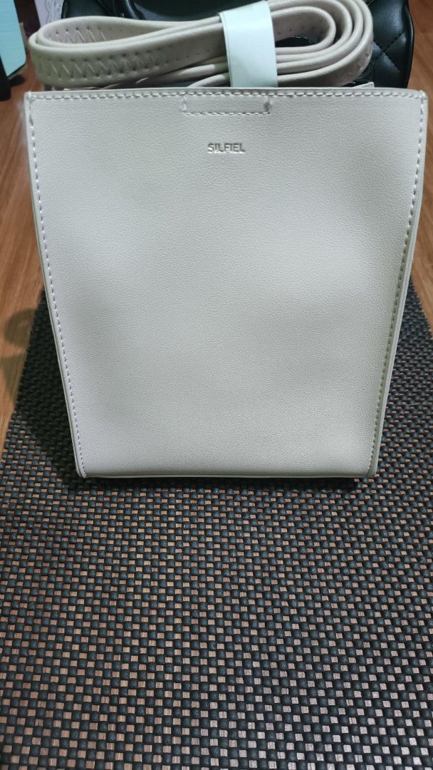 SILFIEL Beige Leather Bucket Bag (Category: Luxury Bags & Wallets) located in Manila. Submitted by akosijapok (Listing ID 1458731447, Image 1). Description: - Brand: SILFIEL - Color: Beige - Material: Genuine Leather - Features: Top handle, detachable strap, magnetic snap closure - Design: Clean and simple bucket bag style - Condition: Excellent, still contains original paper stuffing Design Features: Silhouette: It has a structured, rectangular 