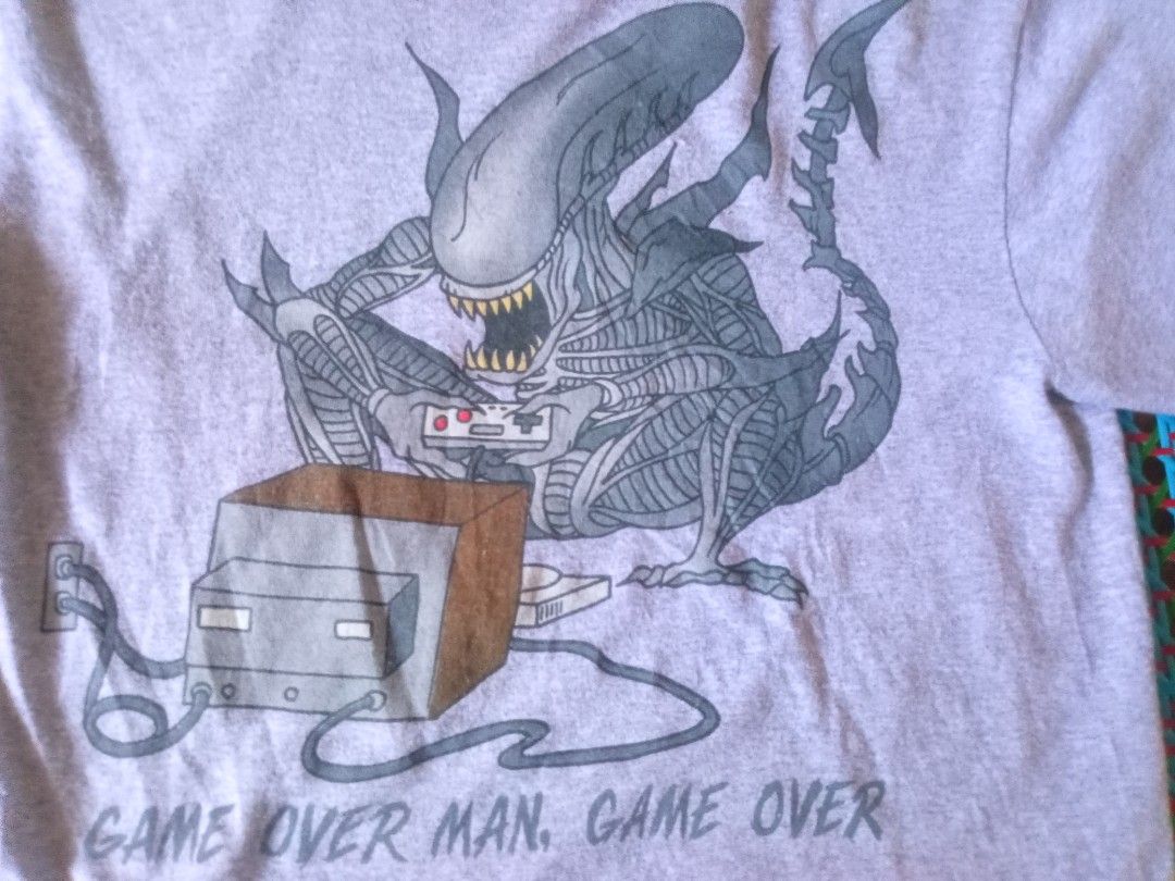 Aliens "Game Over Man" T-Shirt (Category: Tshirts & Polo Shirts ) located in Manila. Submitted by boot_tdm (Listing ID 1453708104, Image 2). Description: - Grey t-shirt with a unique Aliens graphic - Features the Xenomorph playing a video game - Text reads "Game Over Man. Game Over." - Made in Mexico - Size Medium (M).