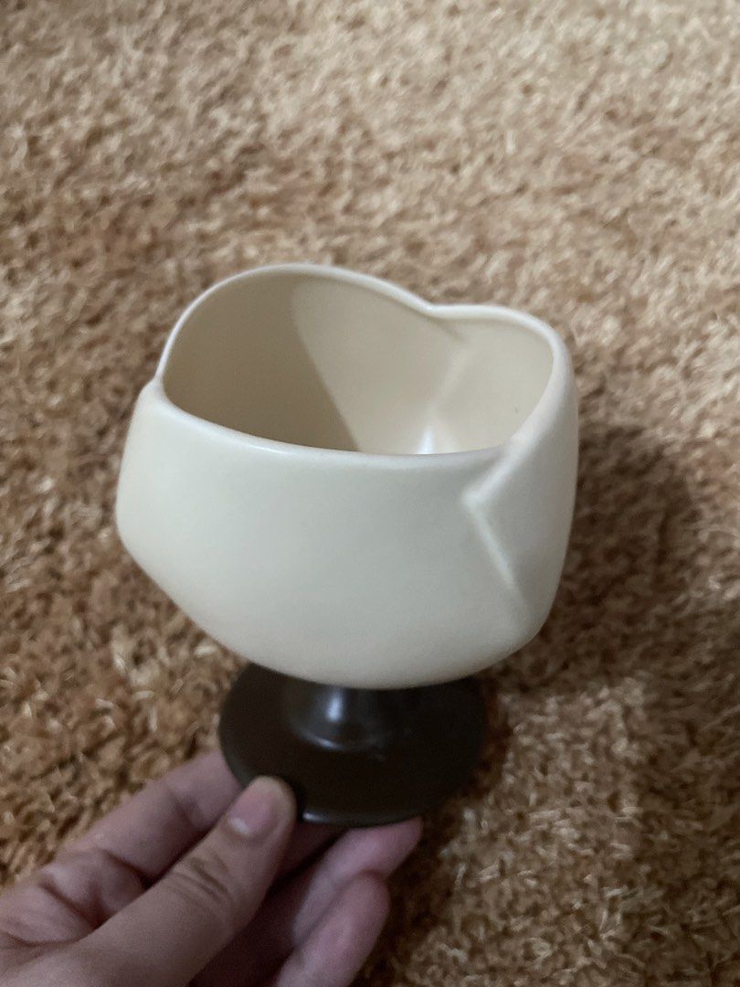 Cream and Brown Ceramic Footed Cup (Category: Coffee & Tea Tableware) located in Guiguinto. Submitted by beatan13 (Listing ID 1453762214, Image 1). Description: - Unique cream-colored cup with a distinct brown base. - Features an unusual heart or egg-like shape. - Ideal for storing small items or as a decorative accent. - Perfect for adding charm to your desk or shelf. - Stands approximately X inches tall..