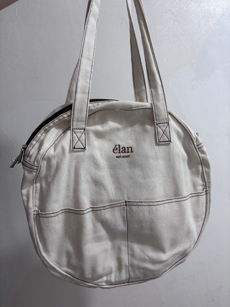 Élan est 2020 Canvas Round Tote Bag (Category: Tote Bags) located in Quezon City. Submitted by makeitkmn (Listing ID 1453747090, Image 1). Description: - Brand: Élan - Color: Cream - Material: Canvas - Style: Round Tote Bag - Closure: Zip - Exterior Pockets: Two front pockets - Stitching Detail: Dark brown - Ideal For: Everyday use - Features: Spacious enough for essentials.