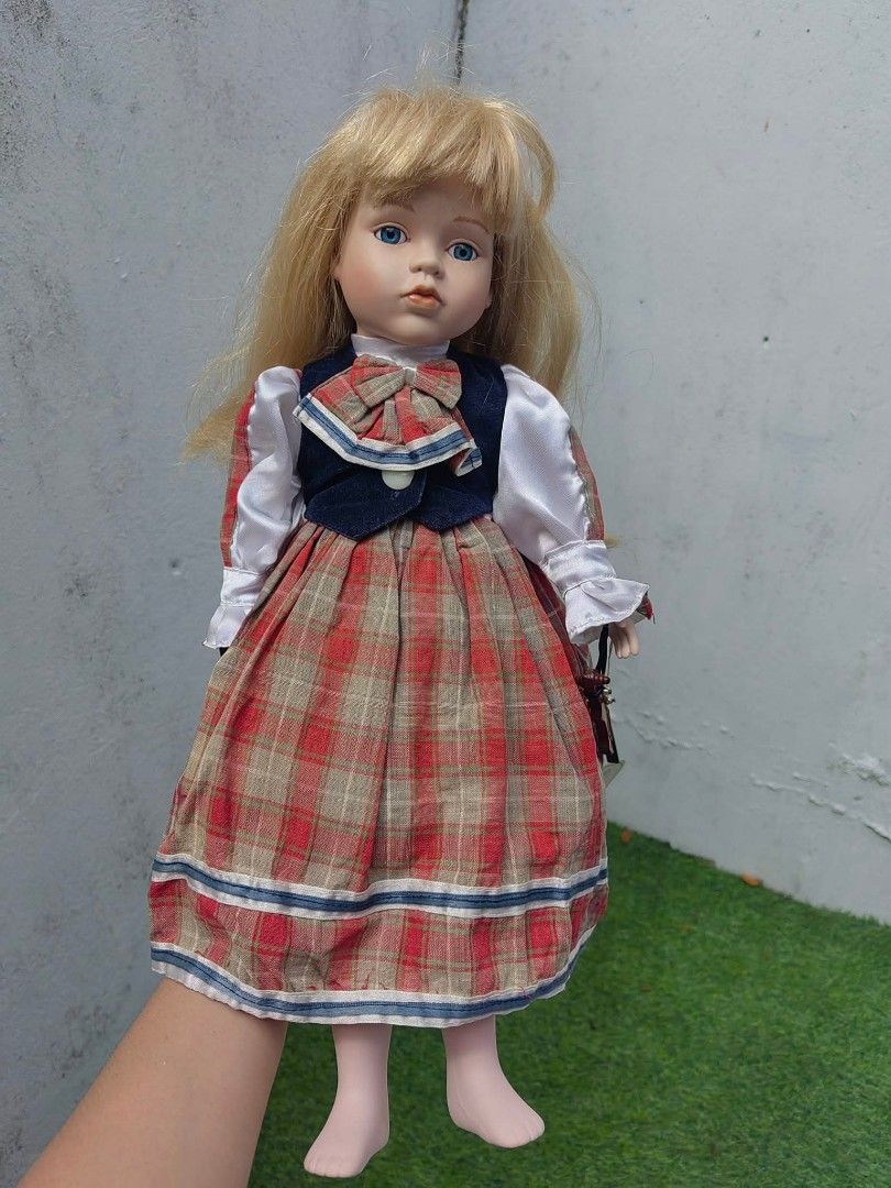 Porcelain Doll (Category: Figurines & Statues) located in Cebu City. Submitted by dudes_villanueva (Listing ID 1453672791, Image 1). Description: Porcelain Doll Brand: Leonardo Collector's 📌 The doll has fine porcelain bisque skin, painted facial accents, glass-like blue eyes, synthetic blonde hair with bangs, and bare feet. 📌 She is styled in a traditional Victorian- or European-inspired outfit, featuring a red and beige tartan plaid pinafore 