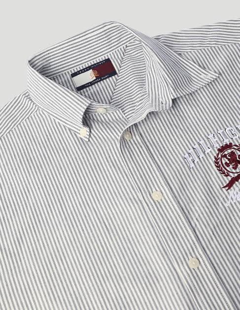 Tommy Hilfiger Striped Button-Down Shirt with Crest Logo (Category: Tshirts & Polo Shirts ) located in Kidapawan. Submitted by azythrift (Listing ID 1453648970, Image 2). Description: - Classic Tommy Hilfiger button-down shirt - Features thin grey and white stripes - Embroidered Tommy Hilfiger crest logo on chest - Striped detail on cuffs - Sharp, clean look - Ideal for casual or smart-casual occasions.