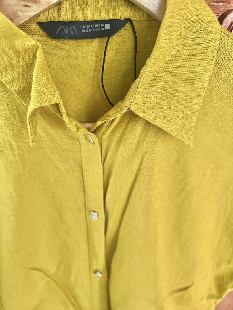 ZARA Mustard Yellow Tie Front Shirt (Category: Shirts) located in San Fernando. Submitted by prettyfinds2021 (Listing ID 1453680014, Image 2). Description: - ZARA Mustard Yellow Shirt - Style: Short sleeves with rolled cuffs - Features: Button-down front, adjustable waist tie - Fabric: Slight sheen for a touch of elegance.