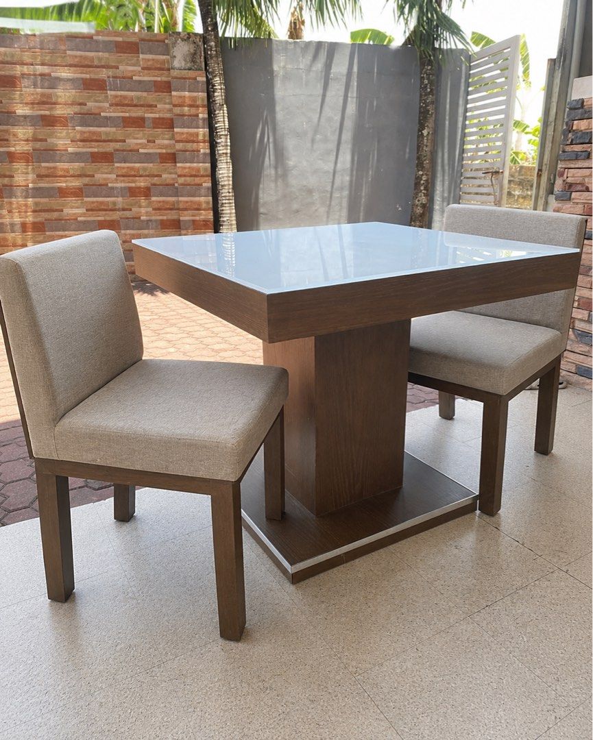Square Glass Top Dining Table with 2 Chairs (Category: Tables & Sets) located in Manila. Submitted by dangiii.24 (Listing ID 1453999186, Image 1). Description: - Modern square dining table with a sleek glossy white top. - Features a stylish wood-look pedestal base. - Comes with two comfortable upholstered chairs in a neutral beige fabric. - Chairs have wooden legs that complement the table's base. - Perfect for small dining spaces, breakfast nook