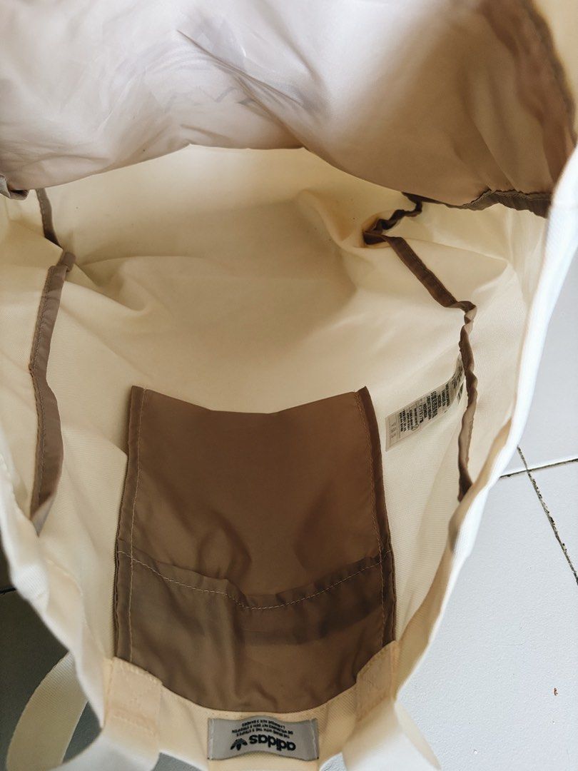 Adidas Java Tote Bag (Category: Sling Bags) located in Singapore. Submitted by BakerTed (Listing ID 1454029593, Image 2). Description: - Cream colored tote bag - Iconic red Adidas trefoil logo - 'JAVA' text detail - Zippered front pocket for secure storage - Internal smaller pocket for organization - Comfortable handles for easy carrying - Perfect for everyday use.