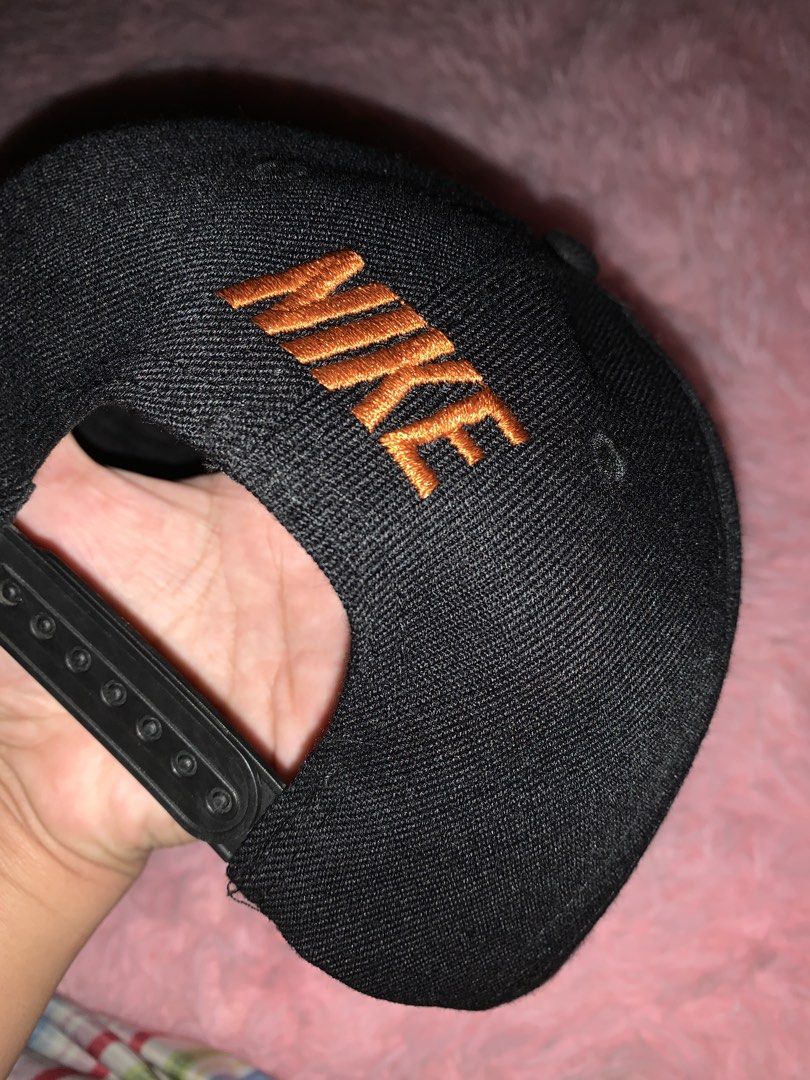 Nike Snapback Cap - Black with Orange Swoosh (Category: Caps & Hats) located in Binan City. Submitted by kariray_shop (Listing ID 1454065965, Image 2). Description: - Classic black Nike snapback cap - Iconic orange Nike swoosh logo - 'NIKE' embroidered in orange on the side - Unique 'REAL FIRE' branding inside - Adjustable snap closure for a custom fit.