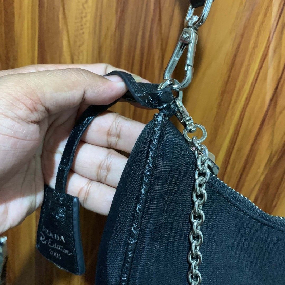 Prada Re-Edition 2005 Nylon Shoulder Bag Black (Category: Luxury Bags & Wallets) located in Carmen. Submitted by ar_thrift00 (Listing ID 1454129475, Image 3). Description: - Prada Re-Edition 2005 shoulder bag - Chic black nylon material - Elegant silver chain detail - Iconic Prada logo prominently displayed on the front - 'PRADA' branding on the shoulder strap - Shows some minor signs of wear on the strap attachment point.