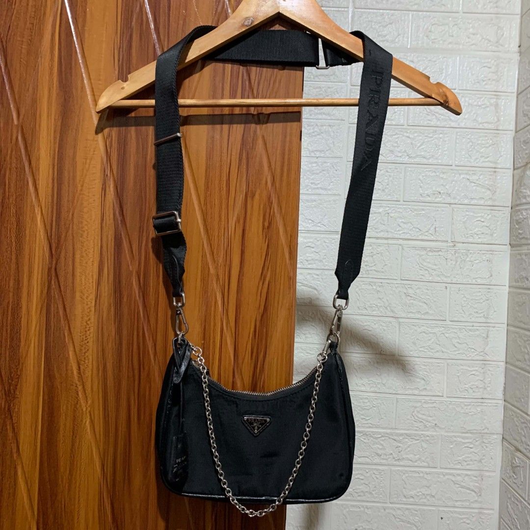 Prada Re-Edition 2005 Nylon Shoulder Bag Black (Category: Luxury Bags & Wallets) located in Carmen. Submitted by ar_thrift00 (Listing ID 1454129475, Image 1). Description: - Prada Re-Edition 2005 shoulder bag - Chic black nylon material - Elegant silver chain detail - Iconic Prada logo prominently displayed on the front - 'PRADA' branding on the shoulder strap - Shows some minor signs of wear on the strap attachment point.