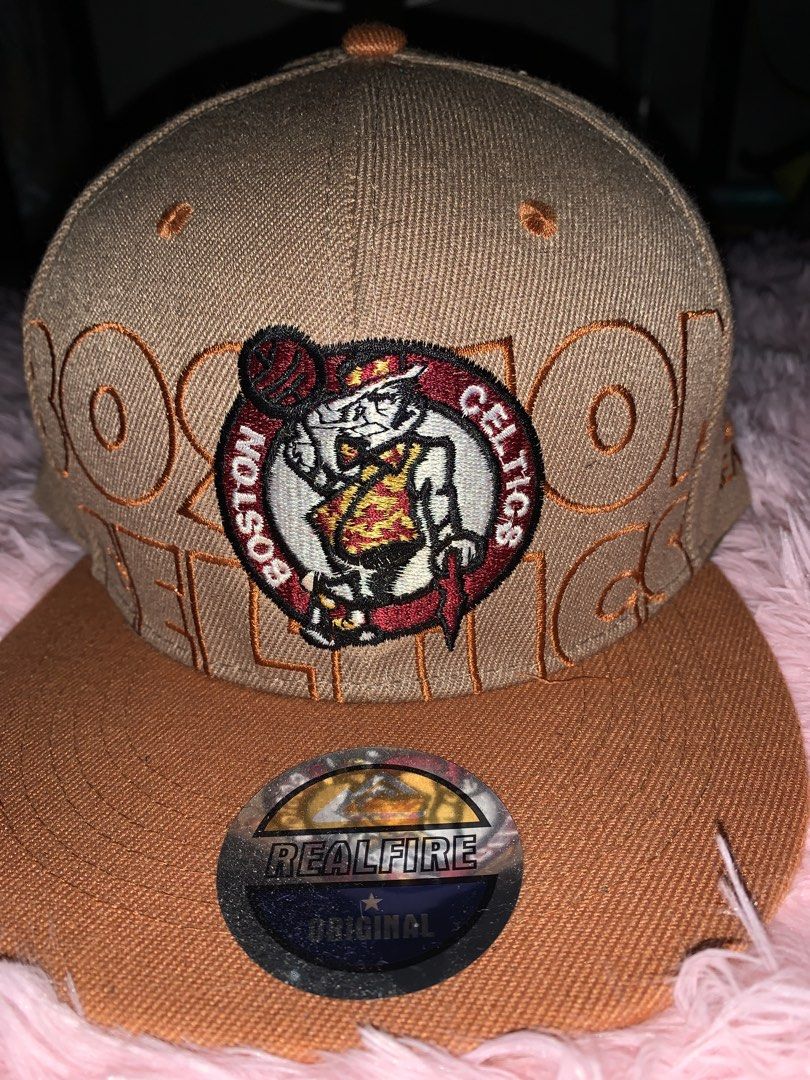 Real Fire Boston Celtics Snapback Cap (Category: Caps & Hats) located in Binan City. Submitted by kariray_shop (Listing ID 1454066140, Image 1). Description: - Brown snapback cap with official Boston Celtics logo - 'Celtics' embroidered on the back - Real Fire brand, original design - Adjustable strap for a comfortable fit - Perfect for any Boston Celtics fan.