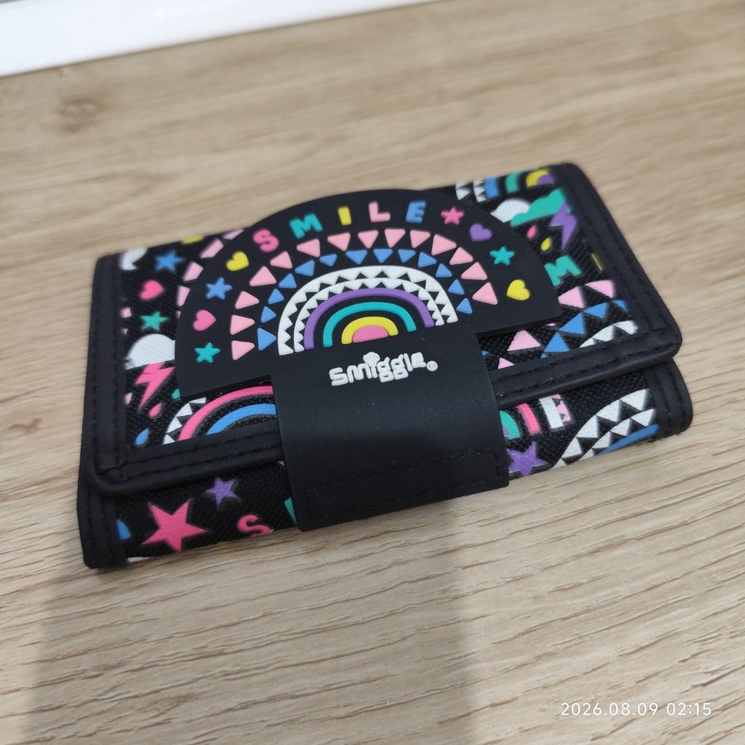 Smiggle Wallet Rainbow (Category: Wallets & Card holders) located in Paranaque City. Submitted by ipuno_ (Listing ID 1454549614, Image 2). Description: - Adorable Smiggle wallet with a vibrant rainbow and smile design. - Classic black base with colorful accents. - Secure and easy velcro closure. - Interior features multiple card slots. - Includes a clear ID window for easy identification. - Convenient zippered pocket for coins. - Ideal for childr