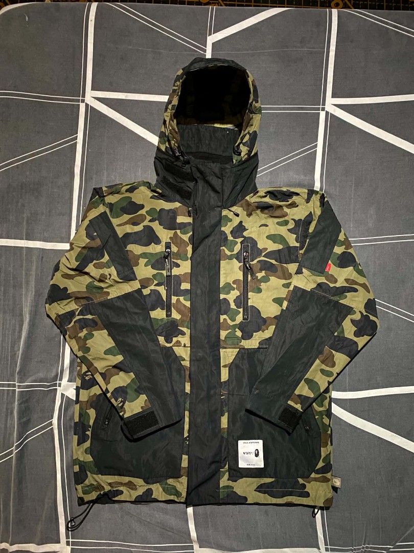 WTAPS/BAPE Camo Hooded Jacket Size X03 (Category: Coats, Jackets and Outerwear) located in Manila. Submitted by raymondrob54698 (Listing ID 1454426560, Image 1). Description: - Authentic WTAPS x BAPE collaboration jacket - Features iconic BAPE camouflage pattern - Stylish black accents on sleeves and hood - Multiple functional zip pockets on the front - Adjustable drawstring hem for a customized fit - Tag reads 'ISSUE, WTAPS/BAPE' - Size X03 87 2