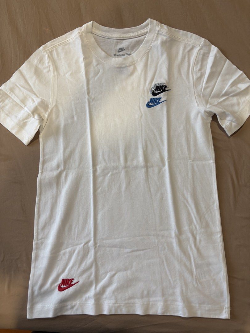 Nike White T-Shirt with Multiple Logos (Category: Tshirts & Polo Shirts ) located in Quezon City. Submitted by aaron.declutters (Listing ID 1454726625, Image 1). Description: - Classic white Nike t-shirt - Features multiple Nike logos on front and back - Main chest logo with blue and black accents - Small red Nike logo on bottom left front - Back features a small embroidered logo with yellow and blue details - Short sleeves and crew neck design -