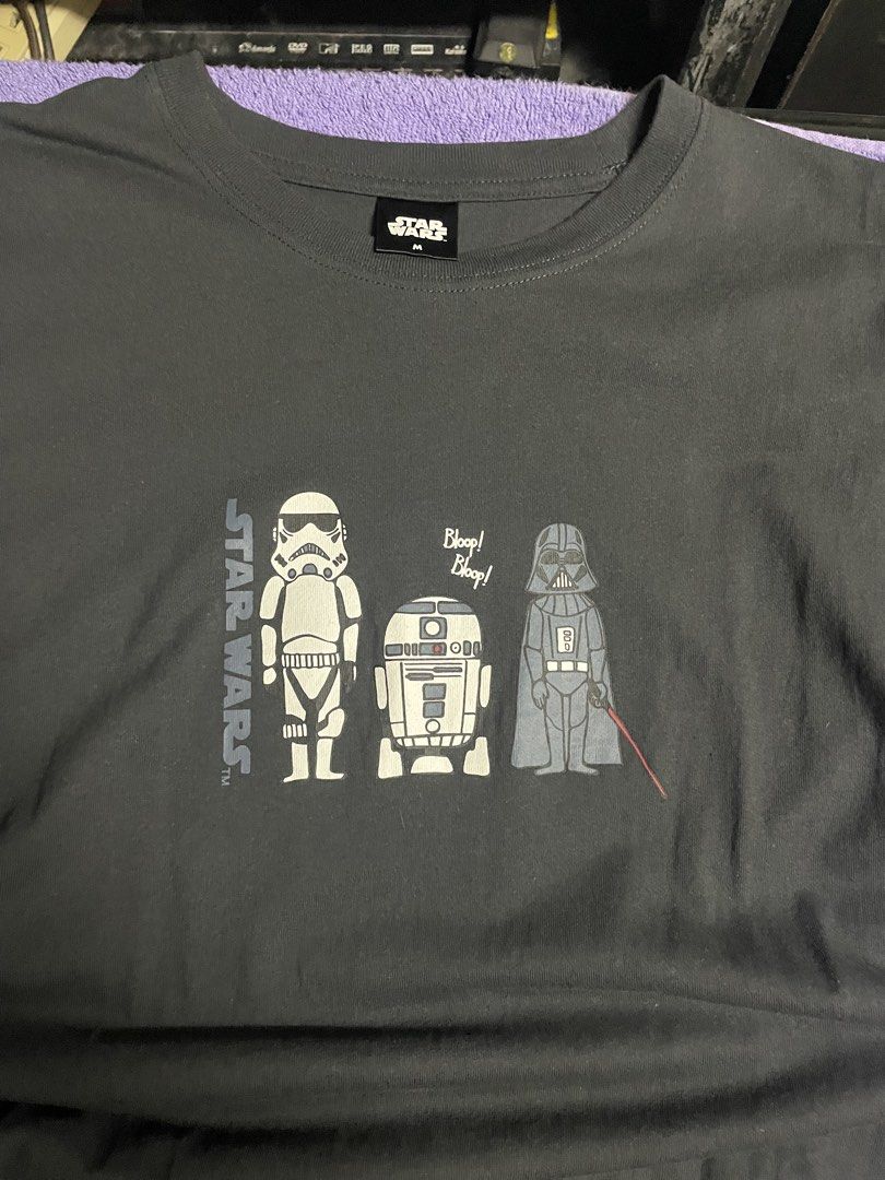 Star Wars Shirt (Category: Activewear) located in Manila. Submitted by 2002kid (Listing ID 1454697409, Image 2). Description: This charcoal grey Star Wars graphic t-shirt features a minimalist cartoon design of a Stormtrooper, R2-D2, and Darth Vader. Design: The shirt showcases a specific cartoon character arrangement with the text “Bloop! Bleep!” above R2-D2.Color: The fabric is a dark charcoal or “ink black” color.Material: It is constructed fr