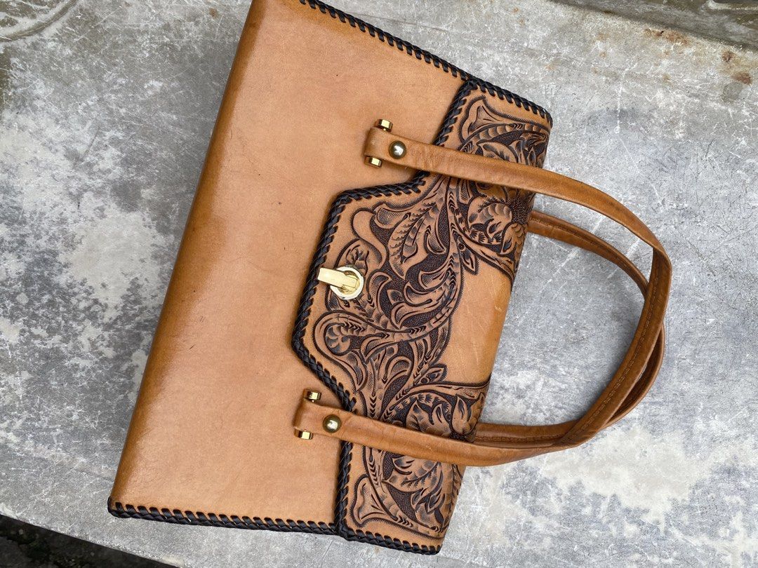 Vintage Tooled Leather Handbag with Lock Closure (Category: Shoulder Bags) located in Manila. Submitted by japansurplusfinds (Listing ID 1454677139, Image 1). Description: - Tan leather handbag - Intricate tooling on front flap - Secure gold-tone lock closure - Braided trim detail - Smooth leather handles - Classic, structured shape - Perfect for carrying essentials with a vintage flair - Neat and consistent stitching.