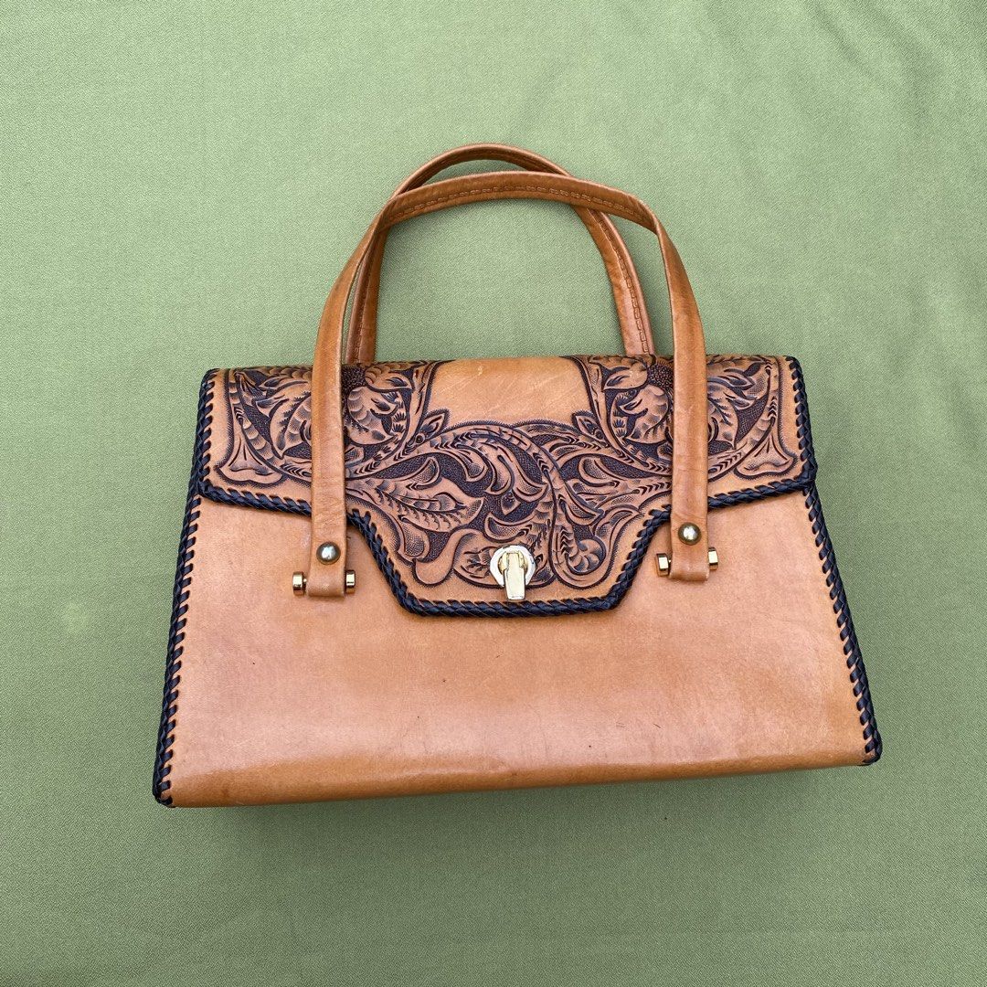 Vintage Tooled Leather Handbag with Lock Closure (Category: Shoulder Bags) located in Manila. Submitted by japansurplusfinds (Listing ID 1454677139, Image 3). Description: - Tan leather handbag - Intricate tooling on front flap - Secure gold-tone lock closure - Braided trim detail - Smooth leather handles - Classic, structured shape - Perfect for carrying essentials with a vintage flair - Neat and consistent stitching.