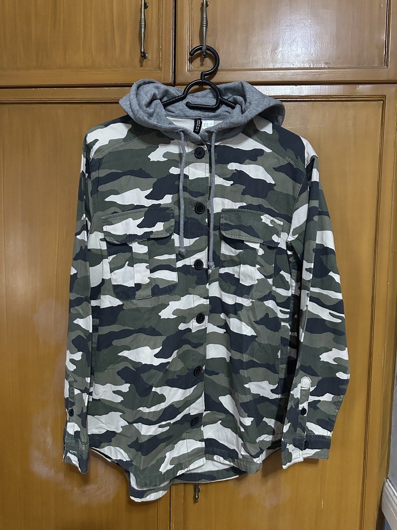 H&M Camo Hooded Jacket (Category: Coats, Jackets and Outerwear) located in Manila. Submitted by dracarysaurzx (Listing ID 1458912250, Image 1). Description: - H&M Camo Print Hooded Jacket - Button-up front with two chest pockets - Long sleeves with button cuffs - Grey hood with adjustable drawstring - Versatile for layering or standalone wear - Pairs well with jeans or joggers.