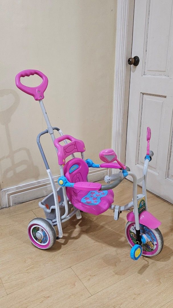 Pink Toddler Tricycle with Parent Handle (Category: Babies & Kids Fashion) located in Paranaque City. Submitted by babythings (Listing ID 1459079349, Image 1). Description: - Pink and grey tricycle perfect for toddlers - Parent push handle for easy steering control - Includes safety bar and footrests for added security - Ideal for outdoor fun and active play - Shows minor scuffs from normal use - Looking for a new loving home!.