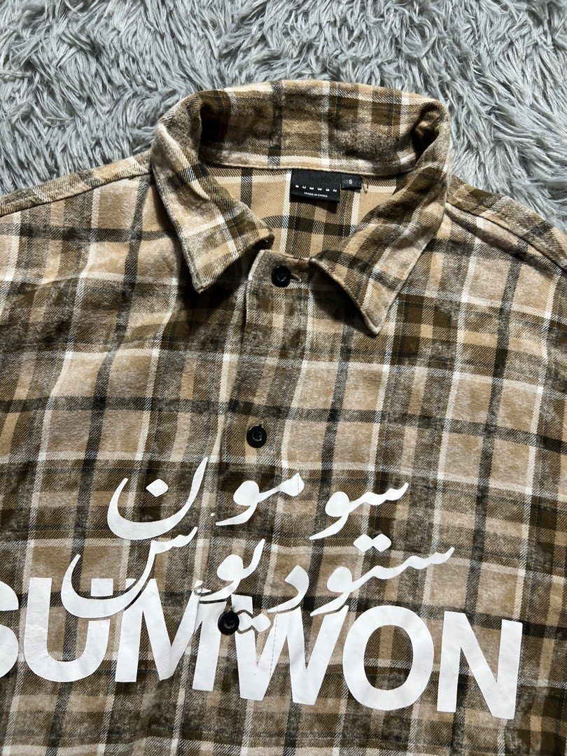 SUMWON Plaid Short Sleeve Button Up Shirt (Category: Tshirts & Polo Shirts ) located in Naga. Submitted by eighttttt (Listing ID 1458918946, Image 2). Description: - Brown and beige plaid short sleeve shirt - Features white Arabic script and 'SUMWON' graphic on the front - Button-up closure - Estimated size S (based on tag) - fit M to L - Ideal for casual wear.