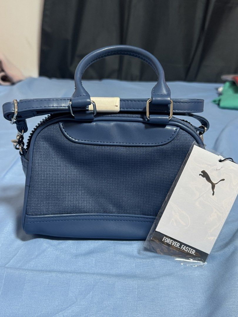 AUTHENTIC Puma Mini Duffle Bag Navy Blue (Category: Cross-body Bags) located in Manila. Submitted by blueishbaddie (Listing ID 1460739339, Image 3). Description: AUTHENTIC Navy blue Puma mini duffle bag - bought in Canada - orig price: $75 CAD w tax / ₱3,394.51 - Features top handles and a detachable shoulder strap - Material is a blend of faux leather and textured fabric - Comes with original tags still attached - Ideal size for carrying your da