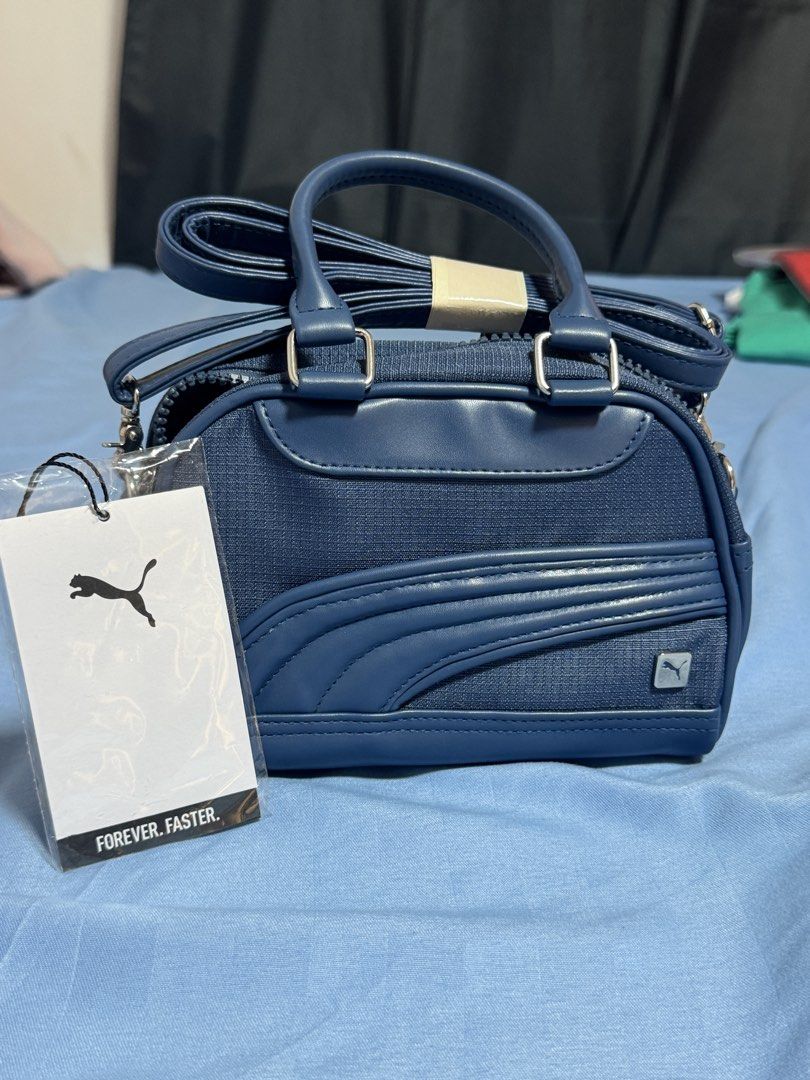AUTHENTIC Puma Mini Duffle Bag Navy Blue (Category: Cross-body Bags) located in Manila. Submitted by blueishbaddie (Listing ID 1460739339, Image 2). Description: AUTHENTIC Navy blue Puma mini duffle bag - bought in Canada - orig price: $75 CAD w tax / ₱3,394.51 - Features top handles and a detachable shoulder strap - Material is a blend of faux leather and textured fabric - Comes with original tags still attached - Ideal size for carrying your da