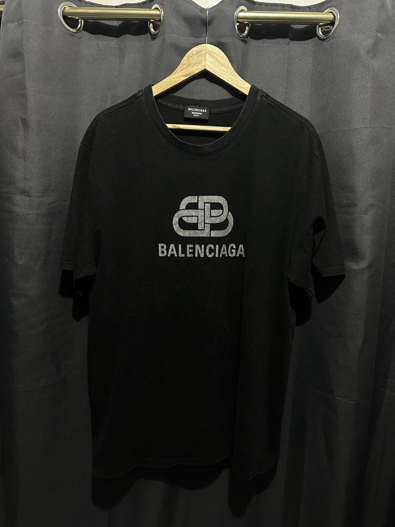 Balenciaga BB Interlocking Logo T-Shirt (Category: Tshirts & Polo Shirts ) located in Buenavista. Submitted by themodernrack (Listing ID 1460800458, Image 1). Description: Brand: Balenciaga Color: Black Style: High-End Streetwear Graphic Tee (Features distress-printed interlocking BB logo and Balenciaga logotype across the chest) Tag Size: Unconfirmed (Fits Medium to Large; see measurements) Condition: Used condition (Fabric fading, neck tag stit