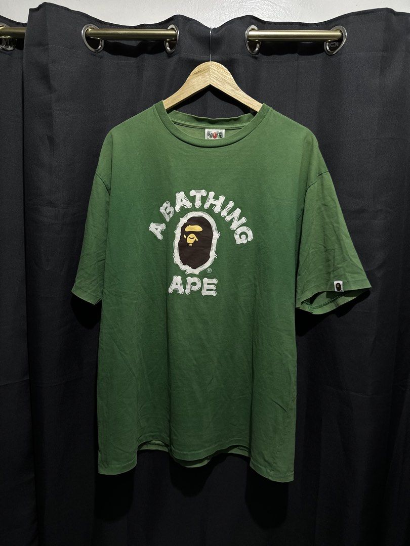 BAPE College Ape Head Graphic Tee (Category: Tshirts & Polo Shirts ) located in Buenavista. Submitted by themodernrack (Listing ID 1460887225, Image 1). Description: Brand: A Bathing Ape (BAPE) Color: Green Style: Short Sleeve Graphic Tee (Classic College Ape Head arch logo front print with back neck “Bape” arch graphic) Tag Size: 3XL (Fits approx. 24” x 29”, see measurements) Condition: Good used condition (Repaired small pinhole, minimal light 