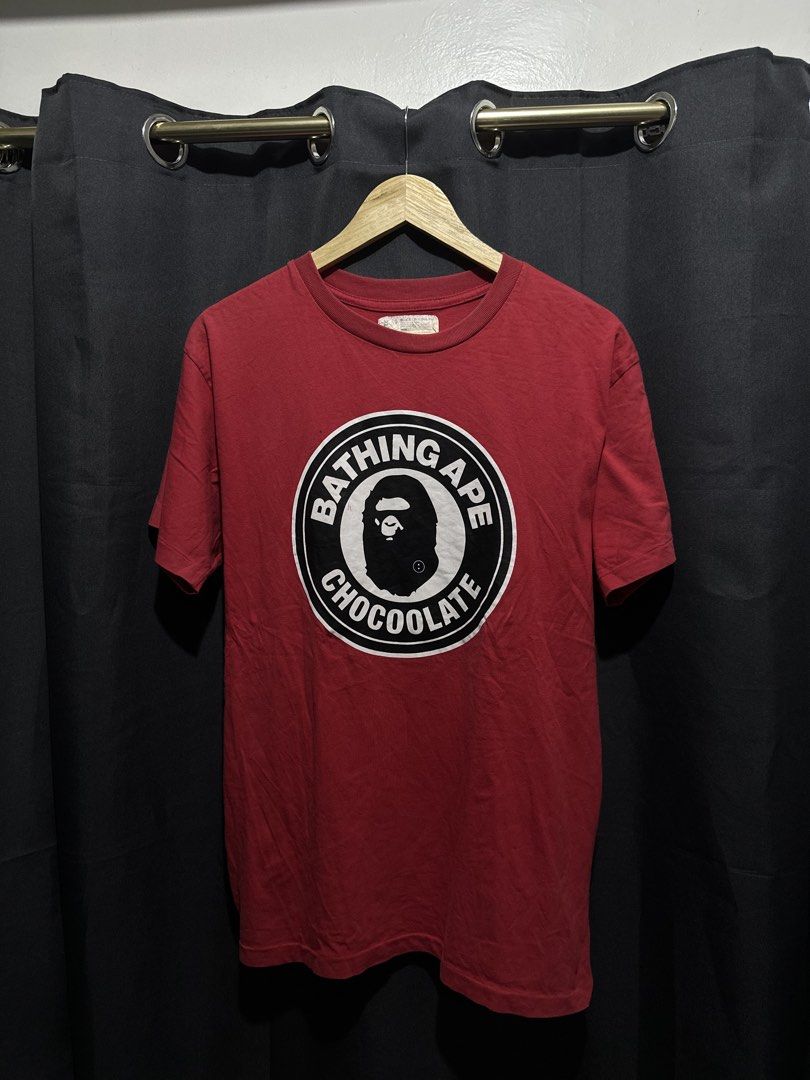BAPE x Chocoolate Circle Seal Ape Head Tee (Category: Tshirts & Polo Shirts ) located in Buenavista. Submitted by themodernrack (Listing ID 1460893845, Image 1). Description: Brand: A Bathing Ape (BAPE) x Chocoolate Color: Red Style: Short Sleeve Graphic Tee (Features circular “Bathing Ape Chocoolate” seal logo print on front) Tag Size: XL (Fits approx. 21” x 29”, see measurements) Condition: Fair used condition (Needs washing; features faint sur