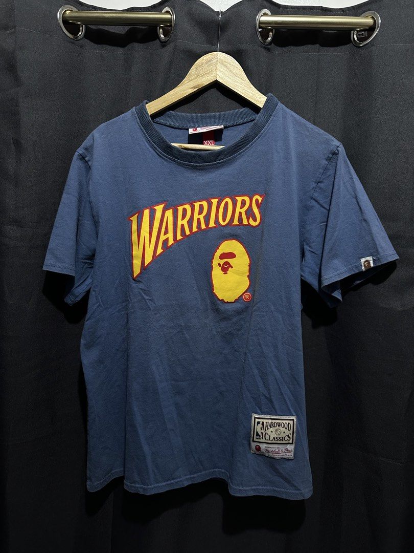 BAPE x Mitchell & Ness NBA Golden State Warriors Tee (Category: Tshirts & Polo Shirts ) located in Buenavista. Submitted by themodernrack (Listing ID 1460894855, Image 1). Description: Brand: A Bathing Ape x Mitchell & Ness Color: Blue Style: Short Sleeve Graphic Tee (Features front Golden State Warriors arch logo with BAPE Ape Head and lower Hardwood Classics jock tag; back printed with “BAPE 93”) Tag Size: XXL (Fits around XL–XXL, see measureme