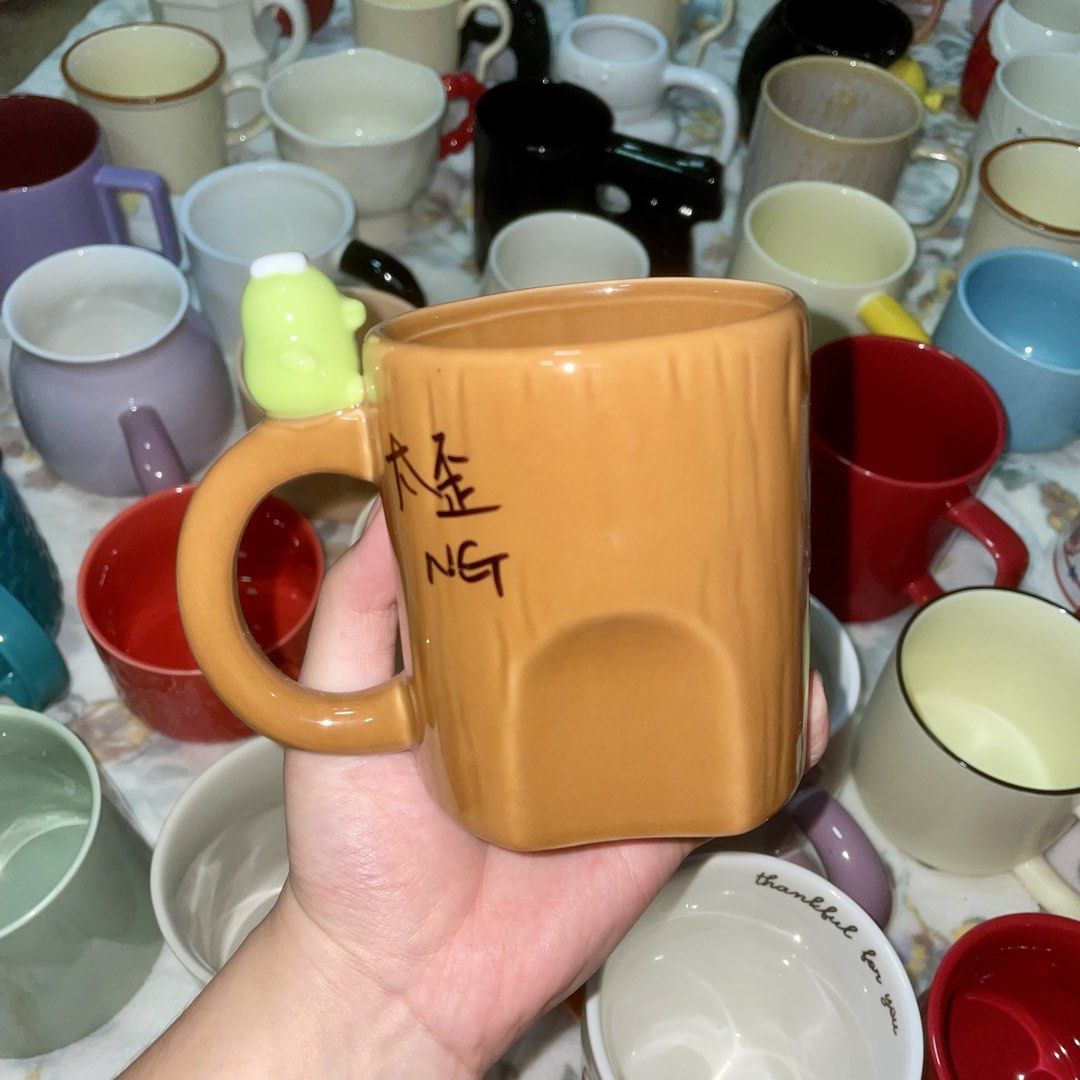 Cute Ceramic Mug with Tree Bark Texture and Green Topper (Category: Coffee & Tea Tableware) located in Valenzuela. Submitted by baekhyunie_pau (Listing ID 1460810306, Image 1). Description: Unique orange-brown mug with tree bark texture and a cute green character topper. Features some writing. Perfect for coffee/tea or display. See other mugs!.