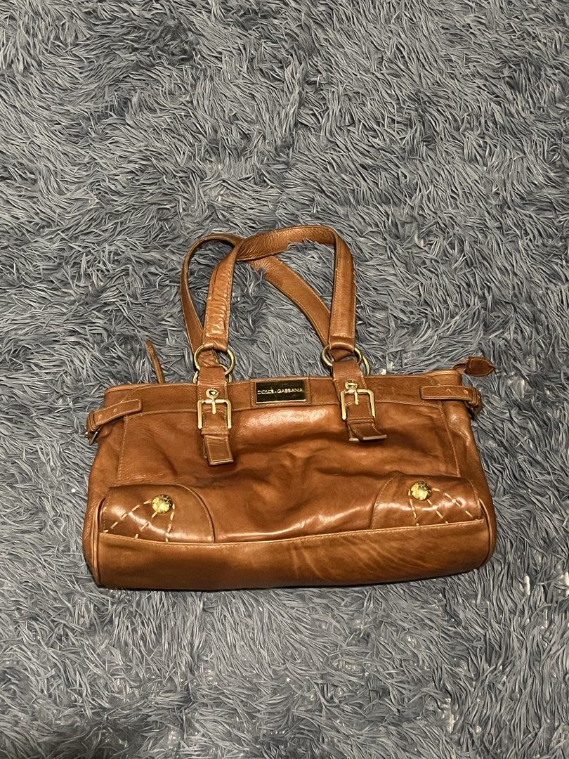 Dolce & Gabbana Brown Leather Tote Bag (Category: Luxury Bags & Wallets) located in Cainta. Submitted by xkengkaix (Listing ID 1460909216, Image 2). Description: - Authentic Dolce & Gabbana brown leather tote bag - Elegant gold hardware and buckle details - Spacious interior with multiple compartments - Shows some signs of wear on the gold plate and leather (adds character!) - Ideal for everyday use, stylish and practical.