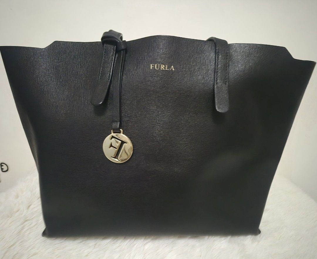 Furla Black Leather Tote Bag - OG (Category: Luxury Bags & Wallets) located in Alaminos. Submitted by tindahanicera (Listing ID 1460772000, Image 1). Description: - Classic black Furla tote bag - Textured leather exterior - Elegant gold hardware (logo charm, zipper pull) - Roomy interior for essentials - Ideal for everyday or travel H - 10.5 in L - 12 in (bottom) 17in (top) W - 6 in Handle - 18 in.