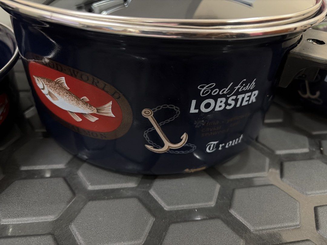 Navy Blue Enamel Cookware Pots with Lids (Category: Cookware & Accessories) located in Quezon City. Submitted by cynlchan (Listing ID 1460773493, Image 3). Description: - 5 pcs navy blue enamel pots 24 cm/18 cm - Each with a glass lid and metal rim/handle - Nautical-themed graphics and text on pots - Largest pot features 'Cod fish LOBSTER Trout' with fish/anchor graphic - Ideal for cooking or as decorative kitchenware.