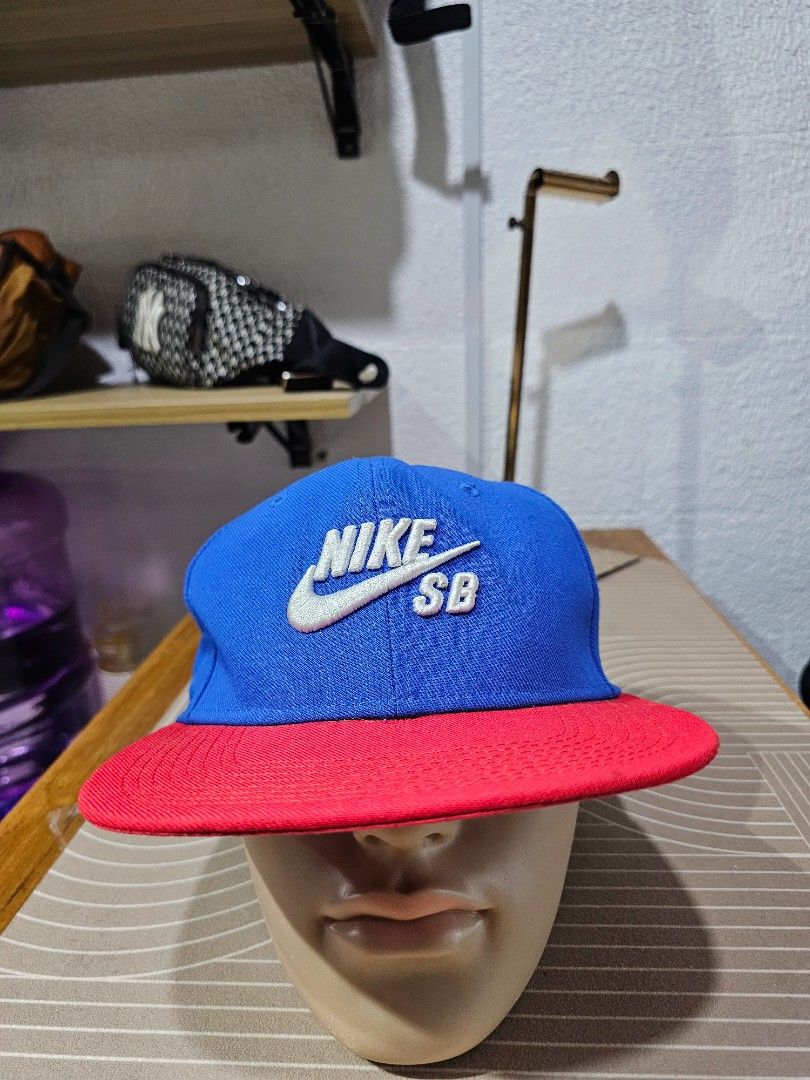Nike SB snapback hat (Category: Caps & Hats) located in Baguio. Submitted by kayeonlineshop (Listing ID 1460759675, Image 1). Description: -blue and red Nike SB snapback hat featuring a prominent white embroidered logo on the front.