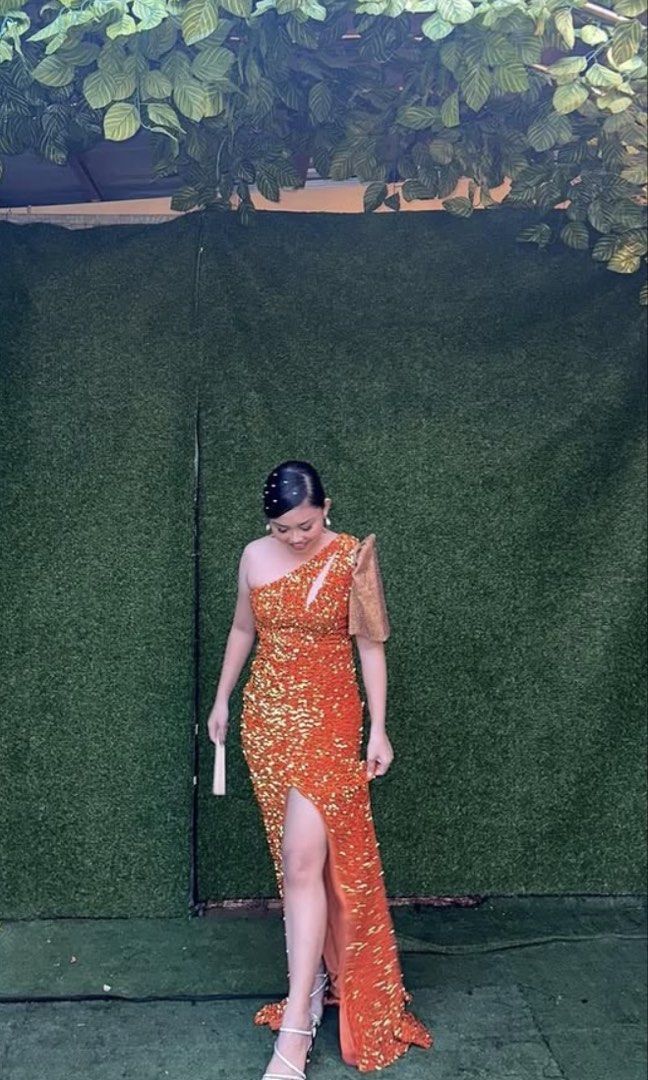Orange Sequin One-Shoulder Gown with High Slit (Category: Evening dresses & gowns) located in Pasig City. Submitted by vivadeclutters (Listing ID 1460813642, Image 1). Description: - Detachable Filipiñana sleeves NOT included - For Sale or Rent - Eye-catching sparkly orange sequin gown - Elegant one-shoulder design - Features a sheer sleeve on one side - Dramatic high slit on the leg - Perfect for formal events, parties, or galas - Worn only once