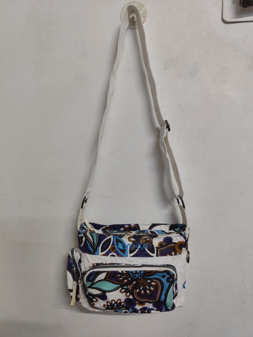 RipCurl Shoulder Crossbody Bag (Category: Sling Bags) located in Compostela. Submitted by fashiondeamar (Listing ID 1460813113, Image 2). Description: Here is a full description of the Rip Curl shoulder/crossbody bag based on the provided images: ​Product Overview ​Brand: Rip Curl (Official Product) ​Type: Crossbody / Shoulder Bag ​Color Palette: White base body featuring a vibrant, multicolored boho-paisley or floral pattern in shades of royal b