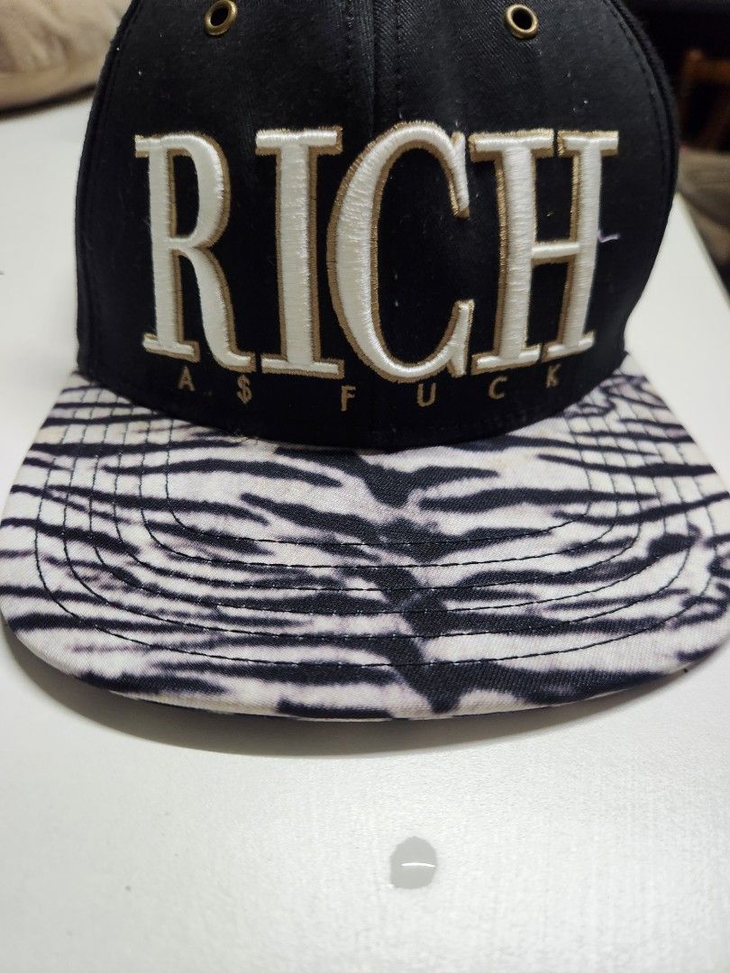 Cayler & Sons "RICH" Snapback Cap Zebra Print Undervisor (Category: Caps & Hats) located in Quezon City. Submitted by amber___18 (Listing ID 1460986709, Image 1). Description: - Brand: Cayler & Sons - Color: Black - Front Embroidery: "RICH" in white and gold - Underside of Brim: Zebra print - Back Embroidery: "Gates Trump LeBron" - Closure: Adjustable snapback.