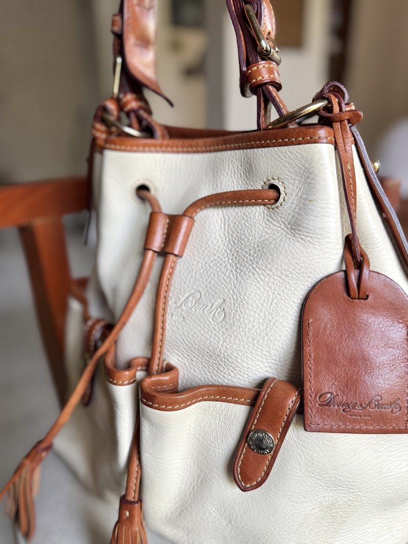 Cream Leather Drawstring Bucket Bag (Category: Luxury Bags & Wallets) located in Bacolod City. Submitted by vintage_vogue6100 (Listing ID 1461072206, Image 2). Description: - Cream leather bucket bag - Brown leather trim - Secure drawstring closure with tassels - Convenient exterior pockets with snap closures - Adjustable shoulder strap for comfortable carrying - Classic and timeless Dooney & Bourke design - Ideal everyday bag for all your essent