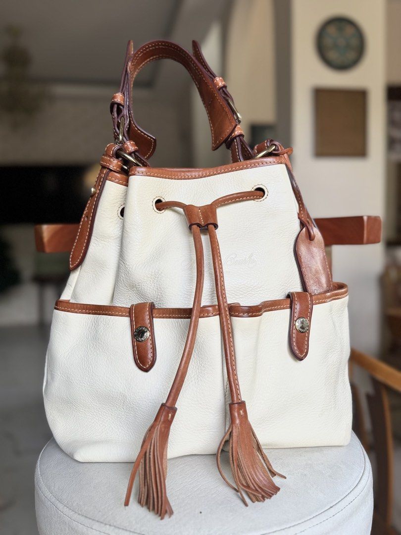 Cream Leather Drawstring Bucket Bag (Category: Luxury Bags & Wallets) located in Bacolod City. Submitted by vintage_vogue6100 (Listing ID 1461072206, Image 1). Description: - Cream leather bucket bag - Brown leather trim - Secure drawstring closure with tassels - Convenient exterior pockets with snap closures - Adjustable shoulder strap for comfortable carrying - Classic and timeless Dooney & Bourke design - Ideal everyday bag for all your essent