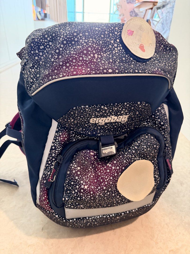 Ergobag Backpack (Category: Babies & Kids Fashion) located in Singapore. Submitted by jojoanneeee (Listing ID 1460941961, Image 1). Description: - Dark blue and purple Ergobag backpack - White speckle pattern - Front zip pocket - Main compartment - Reflective strips for visibility - Two light-colored patches (front & top) - Adjustable straps - Perfect for school use - Original price $200.