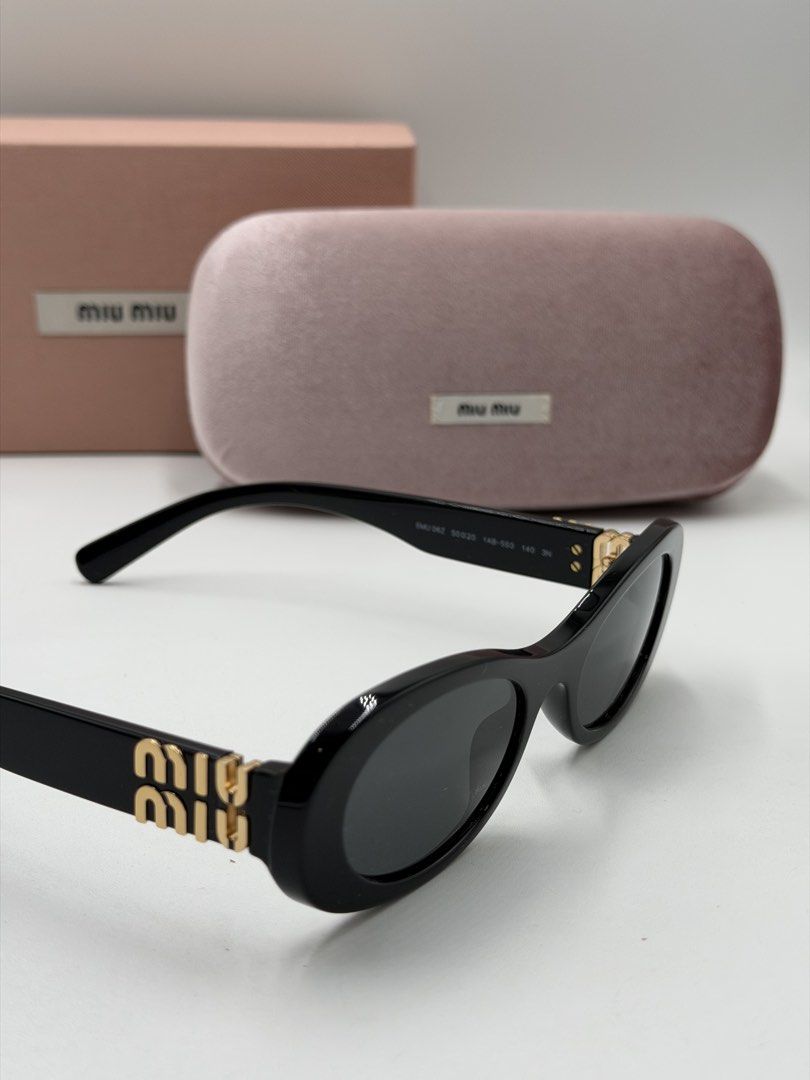 Miu Miu Glimpse (MU 06ZS (Category: Luxury Accessories) located in Quezon City. Submitted by _cmluxephilippines (Listing ID 1460930020, Image 3). Description: Miu Miu Glimpse (MU 06ZS) oval-frame sunglasses, featuring a glossy black acetate frame paired with deep grey/slate tinted lenses. A defining element of this model is the bold, gold-tone openwork Miu Miu logo plaque integrated into the temples.