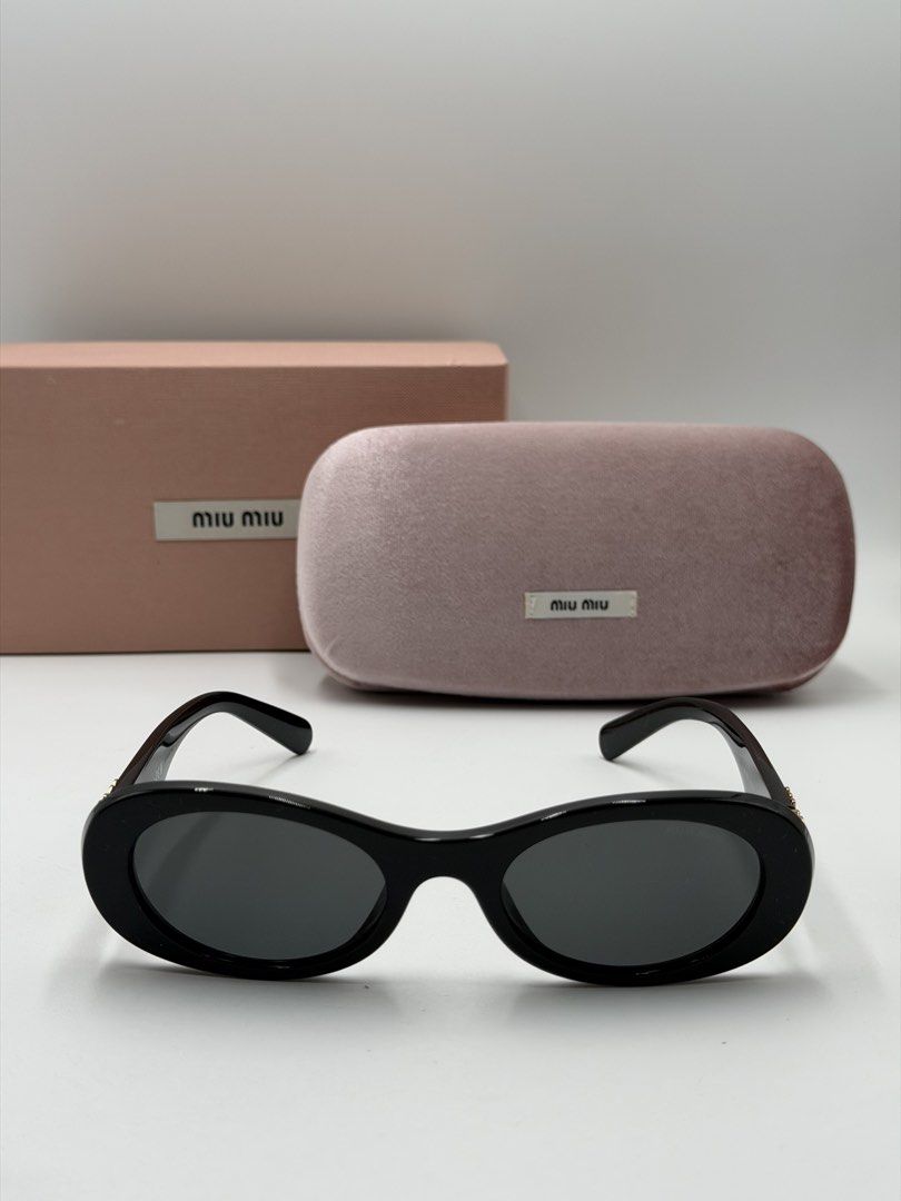 Miu Miu Glimpse (MU 06ZS (Category: Luxury Accessories) located in Quezon City. Submitted by _cmluxephilippines (Listing ID 1460930020, Image 2). Description: Miu Miu Glimpse (MU 06ZS) oval-frame sunglasses, featuring a glossy black acetate frame paired with deep grey/slate tinted lenses. A defining element of this model is the bold, gold-tone openwork Miu Miu logo plaque integrated into the temples.