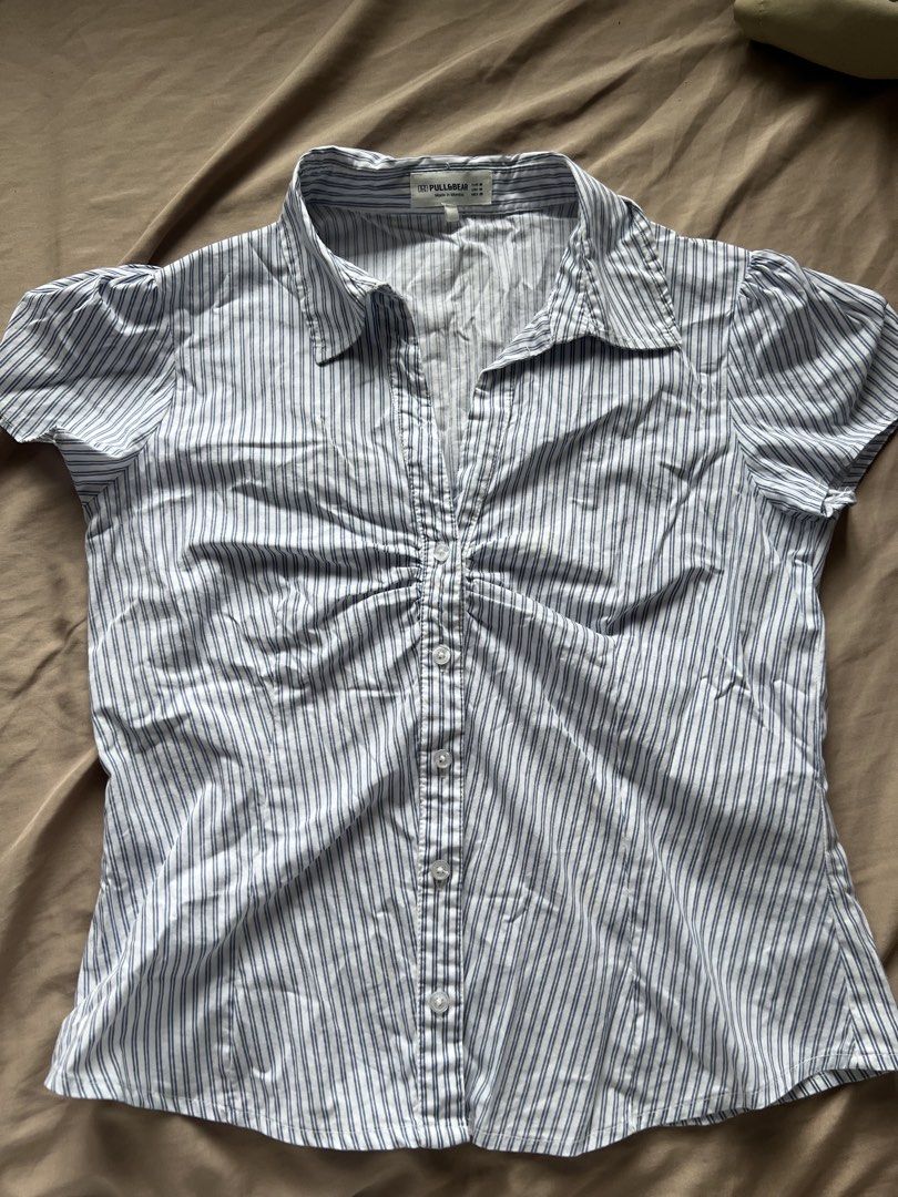 Pull & Bear Striped Button-Up Shirt (Category: Shirts) located in Valenzuela. Submitted by decluttering.manila (Listing ID 1460994860, Image 1). Description: - Classic blue and white pinstripe shirt from Pull & Bear. - Button-up front with a collared neckline. - Short sleeves with a subtle puff detail. - Gathered detail at the bust for a flattering fit. - Size: Medium (M) - Origin: Made in Morocco..