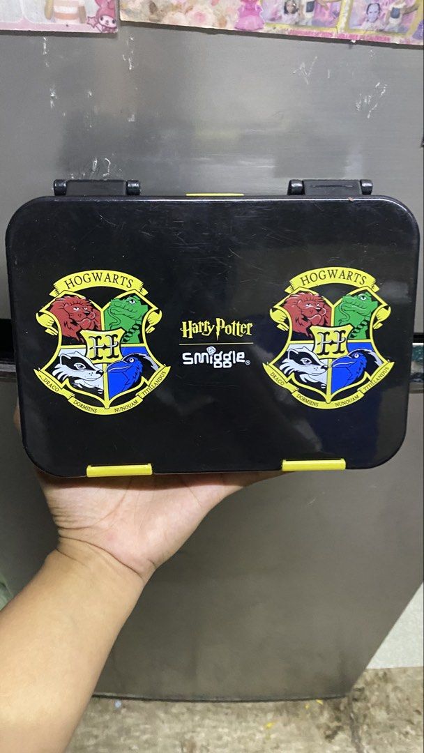 Smiggle Harry Potter Hogwarts Lunch Box (Category: Stationery & School Supplies) located in Manila. Submitted by mariamicaella24 (Listing ID 1461094037, Image 1). Description: - Smiggle Black Lunch Box - Features Harry Potter and Hogwarts crest design - Includes all four house crests - Ideal for school lunches and snacks - Easy to open and close with secure yellow clasps.