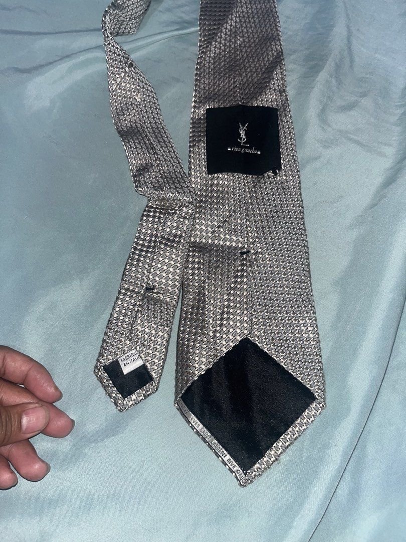 Yves Saint Laurent YSL Tie - Silver Houndstooth Pattern (Category: Ties) located in Tabuk. Submitted by collectors_thrift_shop (Listing ID 1461019972, Image 2). Description: - Silver tie with a sophisticated houndstooth pattern. - Crafted from 100% pure silk. - Proudly manufactured in Italy. - Features the iconic YSL logo on a black label. - A stylish addition to elevate your formal attire..