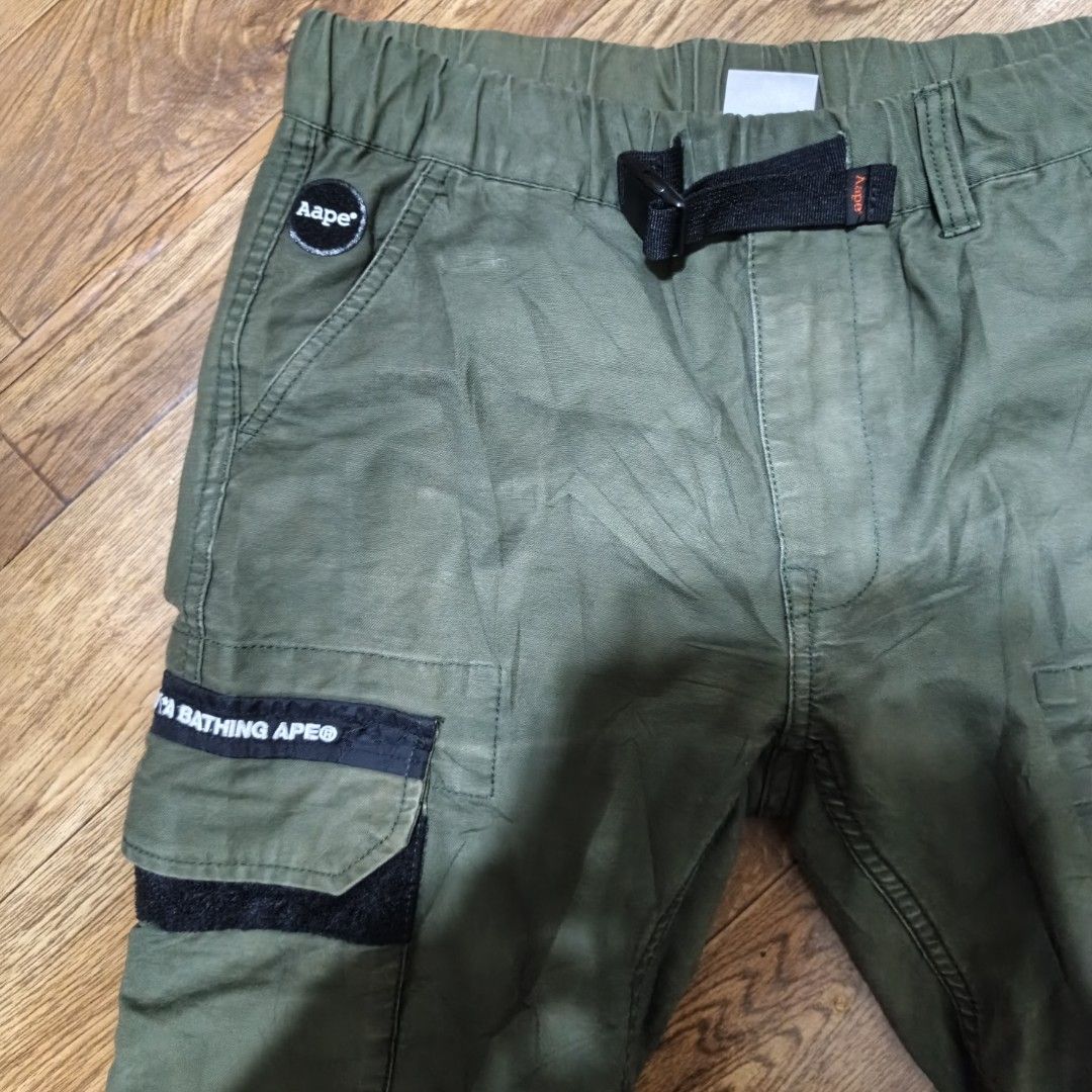 AAPE BY A BATHING APE Cargo Pants Olive Green (Category: Jeans) located in Manila. Submitted by narju1234 (Listing ID 1461124452, Image 2). Description: - Olive green cargo pants from AAPE by A Bathing Ape. - Size S. - Elastic waistband with adjustable belt. - Multiple pockets with secure velcro and button closures. - Signature AAPE branding on leg and back. - Unique 'APES AND PLANET EARTH' graphic detail on the leg..