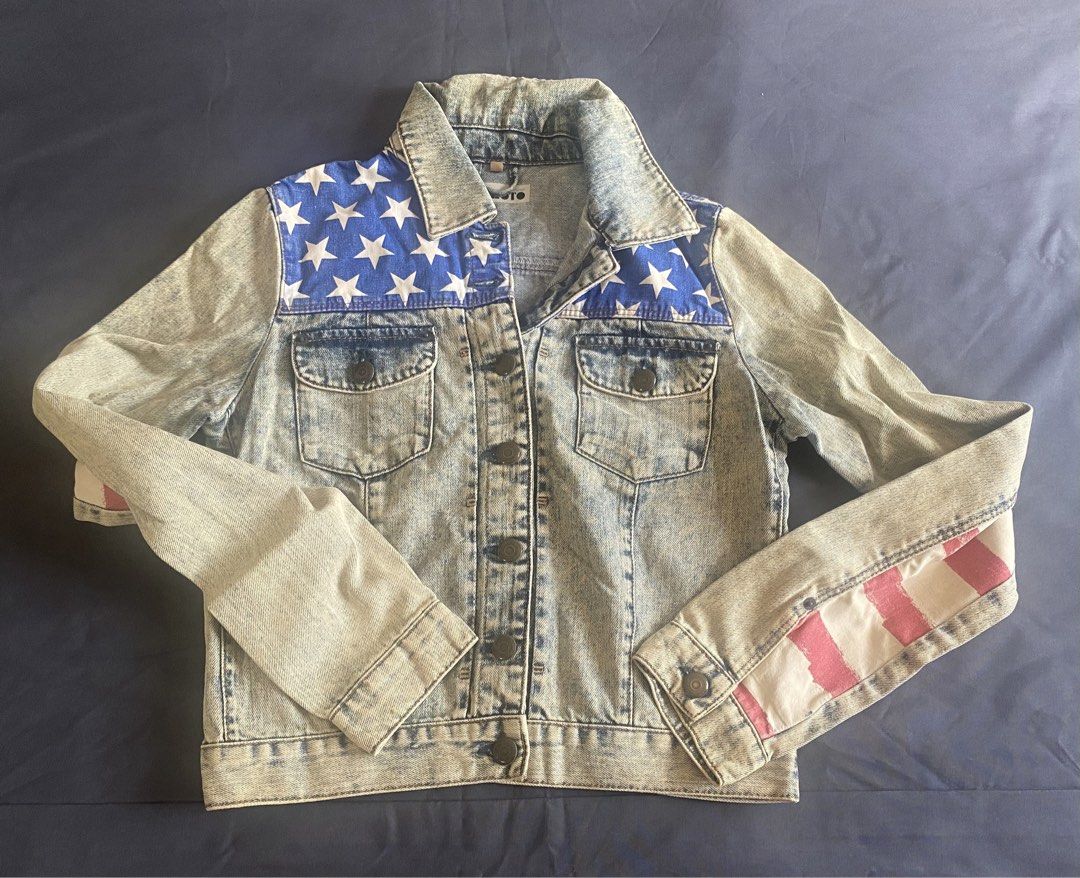 American Flag Denim Jacket (Category: Coats, Jackets and Outerwear) located in Paranaque City. Submitted by axie1206 (Listing ID 1461267235, Image 2). Description: - Classic denim jacket with an eye-catching American flag design. - Features stars on the shoulders for a unique touch. - Stripes adorn the back and sleeves, adding a patriotic flair. - Traditional button-up front closure. - Convenient chest pockets for essentials. - A perfect statemen