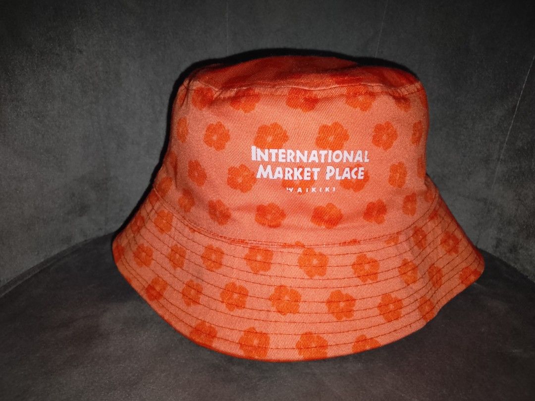 AOP Floral Bucket Hat (Category: Hats & Beanies) located in Binangonan. Submitted by yuristalin888 (Listing ID 1461308132, Image 2). Description: Bring a piece of Hawaiian paradise to your accessory collection with this vibrant orange bucket hat. The hat features a playful, all-over floral pattern in a slightly darker orange hue. Prominently embroidered on the front in white thread is the text "INTERNATIONAL MARKET PLACE" above "WAIKIKI". Crafted